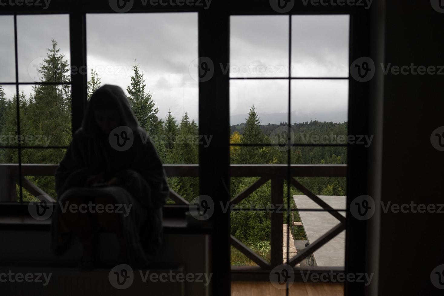 Woman sits on the windowsill and looks at the mountains photo