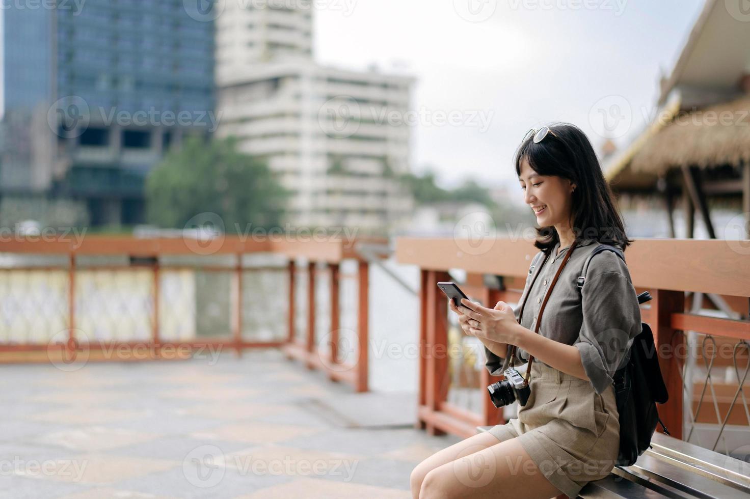 Young Asian woman backpack traveler using mobile phone in express boat pier on Chao Phraya River in Bangkok. photo