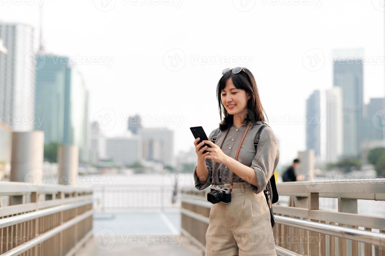 Young Asian woman backpack traveler using mobile phone in express boat pier on Chao Phraya River in Bangkok. photo