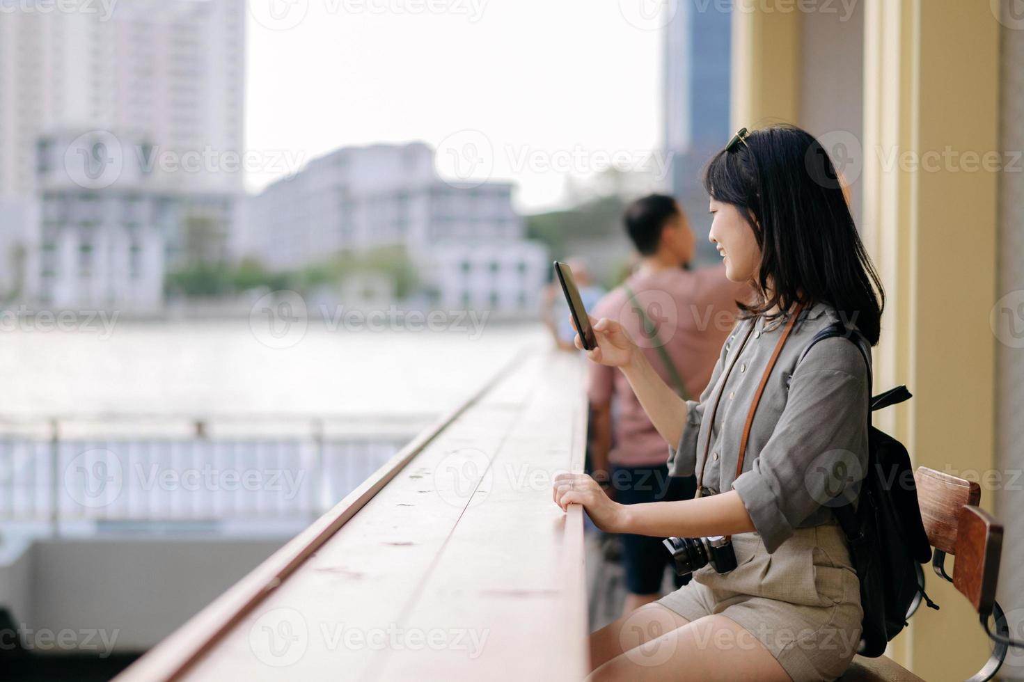 Young Asian woman backpack traveler using mobile phone in express boat pier on Chao Phraya River in Bangkok. photo