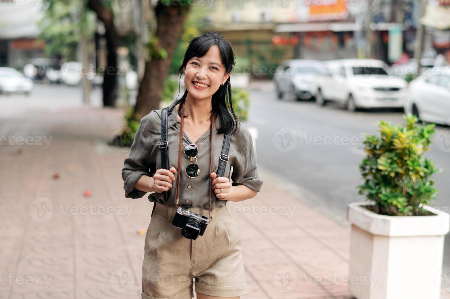 joven asiático mujer mochila viajero disfrutando calle cultural local sitio y sonrisa. viajero comprobación fuera lado calles foto