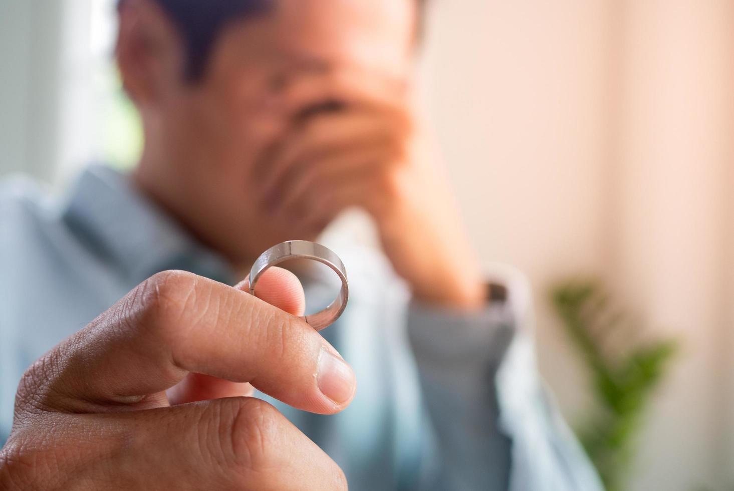 Image of husband crying sadly holding a wedding ring after an argument with his wife and deciding to separate. photo