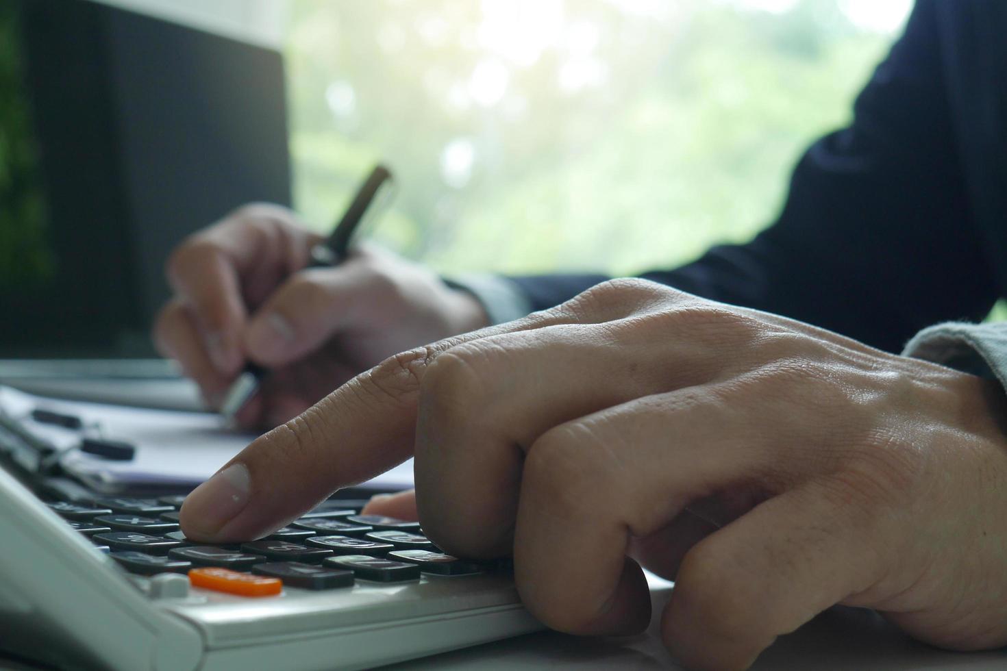 Men use the calculator and take notes with calculations about the expenses at the office. Prepare to submit annual tax photo
