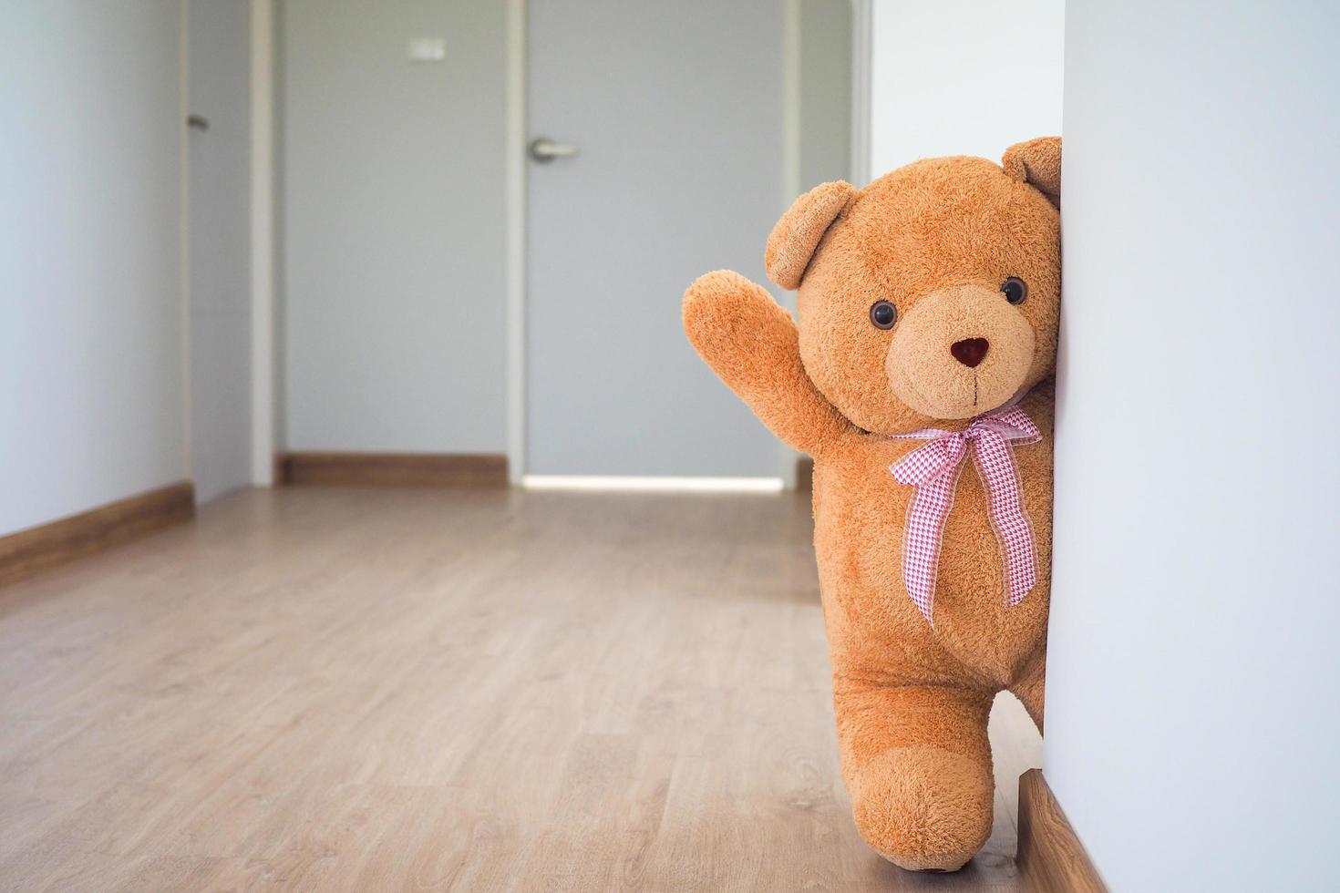 oso de peluche con cabello castaño detrás de la puerta abierta. fondo para niños jugar oso de peluche foto