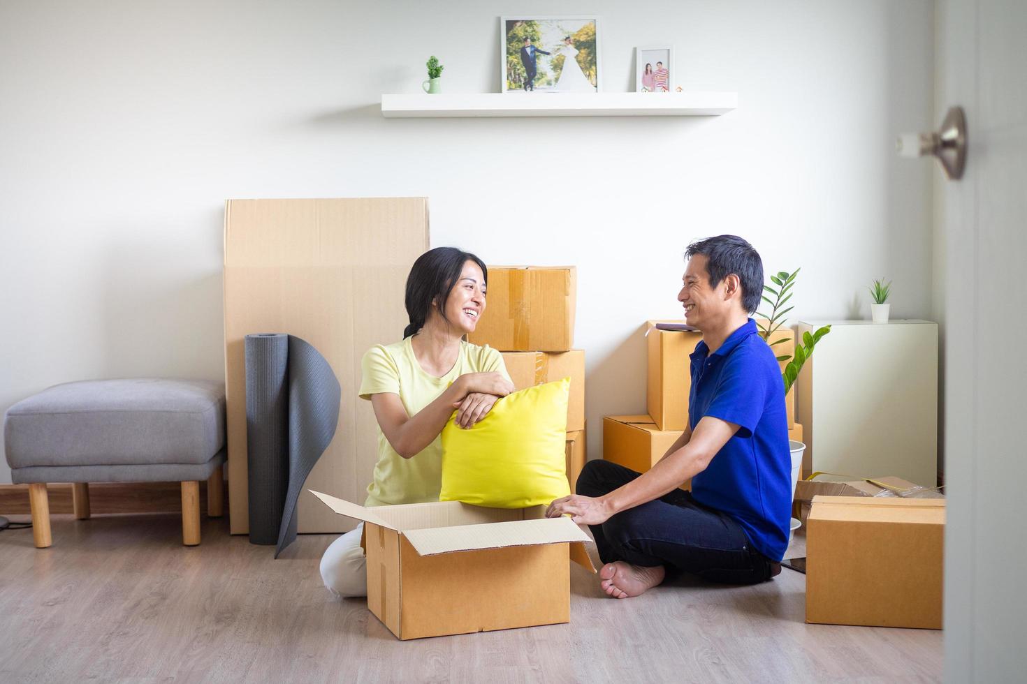 joven sonriente Pareja unión sentado en piso en nuevo hogar con cajas en Moviente día. contento propietarios o inquilinos sólo movido dentro moderno casa. familia reubicación y entrega Servicio concepto. foto