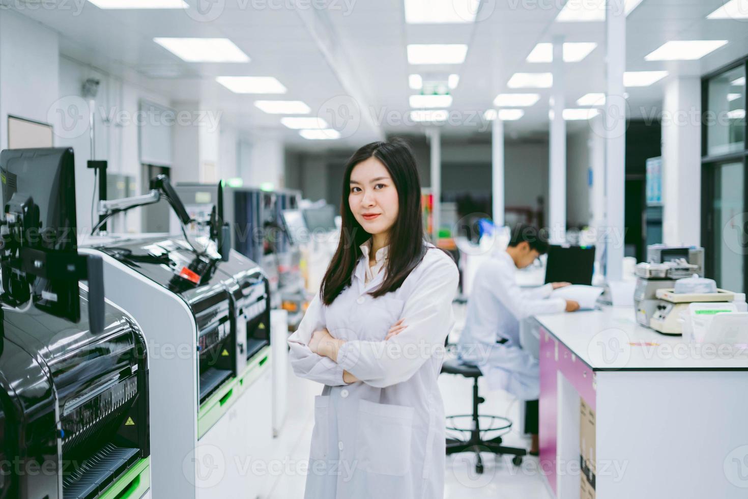 young smiling scientist in white lab coat standing with automation blood analyzer at medical laboratory photo