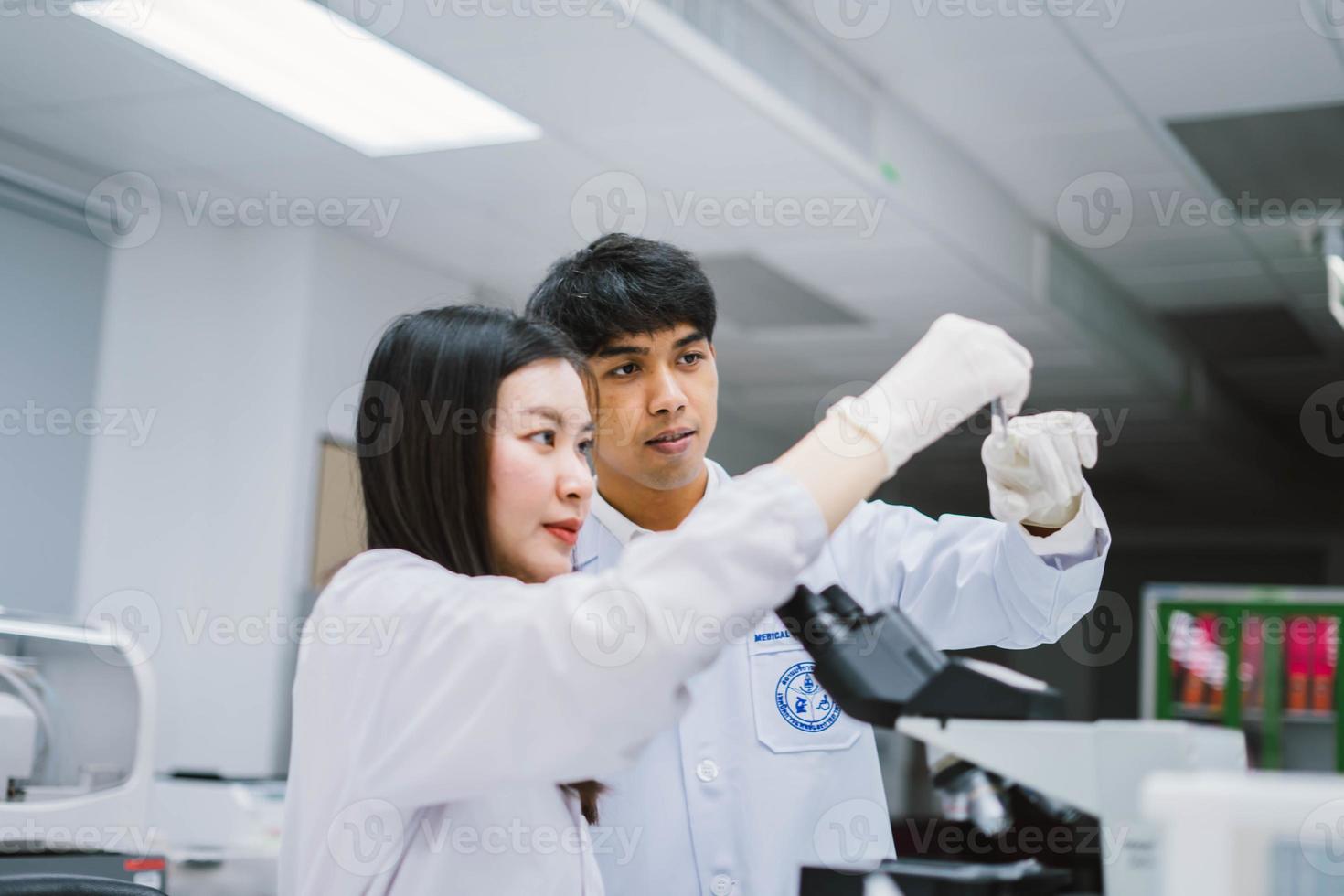 dos jóvenes científicos médicos que miran el tubo de ensayo en el laboratorio médico, seleccionan el enfoque en el científico masculino foto