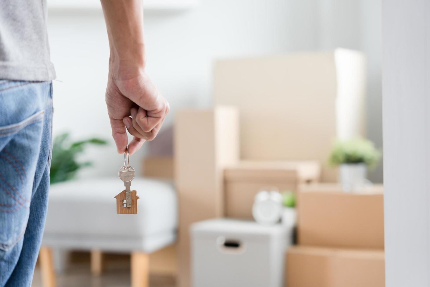 Moving house, relocation. Man hold key house keychain in new apartment, inside the room was a cardboard box containing personal belongings and furniture. move in the apartment or condominium photo