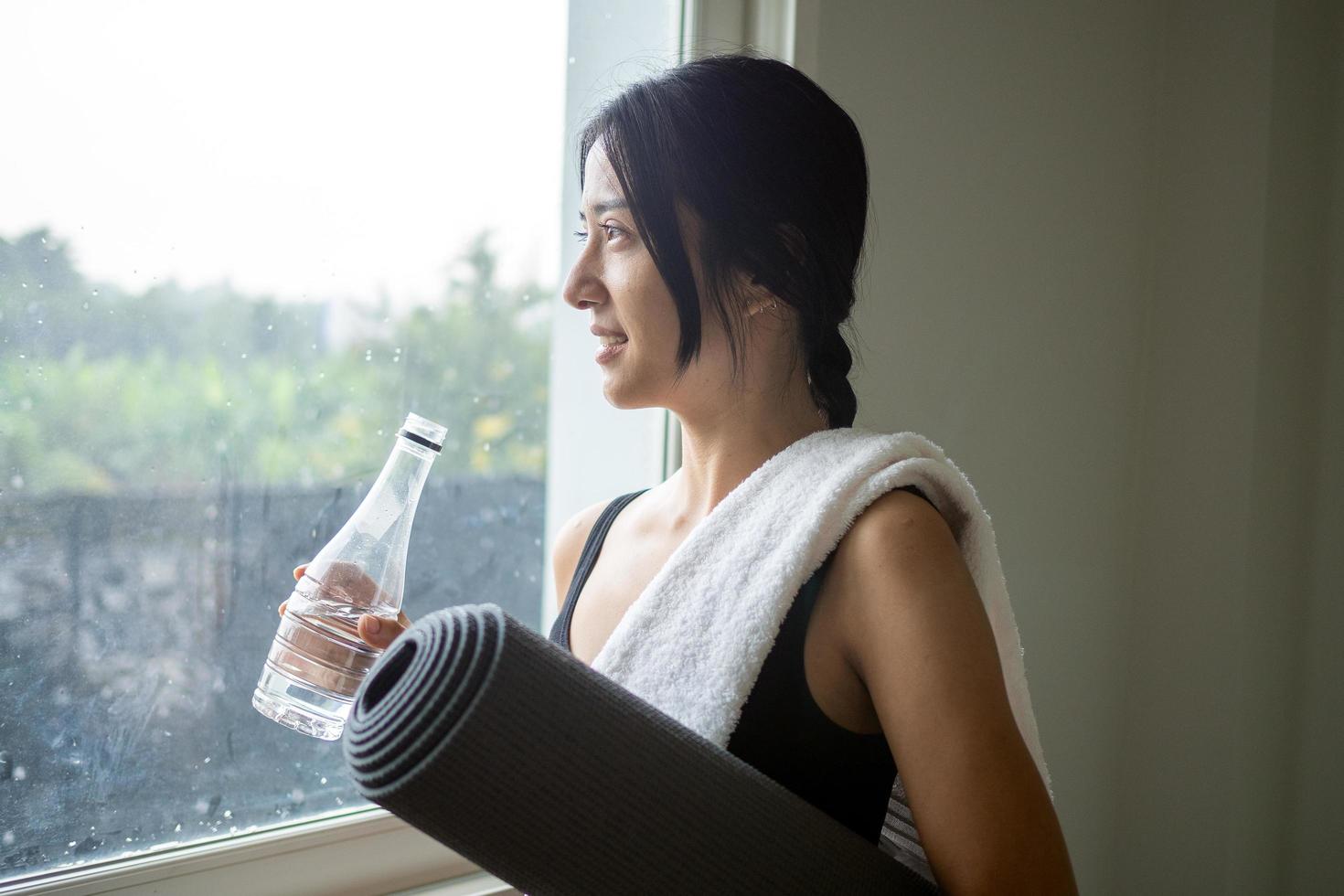 Woman wearing exercise clothes is resting of drinking water after doing yoga in home. photo