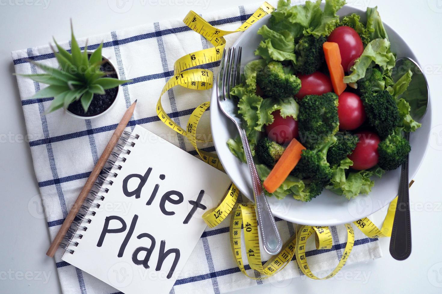 Healthy eating concept. Vegetable salad, food control notebook and tape measure photo