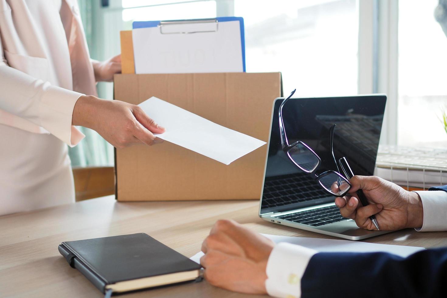The business woman has a brown cardboard box next to her body and sends a letter of resignation to the executive. Include about resignation, job placement and vacancies. photo