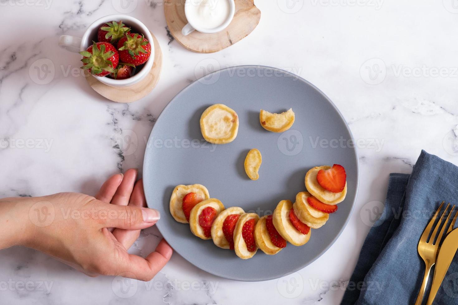 Small pancakes with strawberries in the original serving in the form of a smiley face. Top view. Flat lay photo