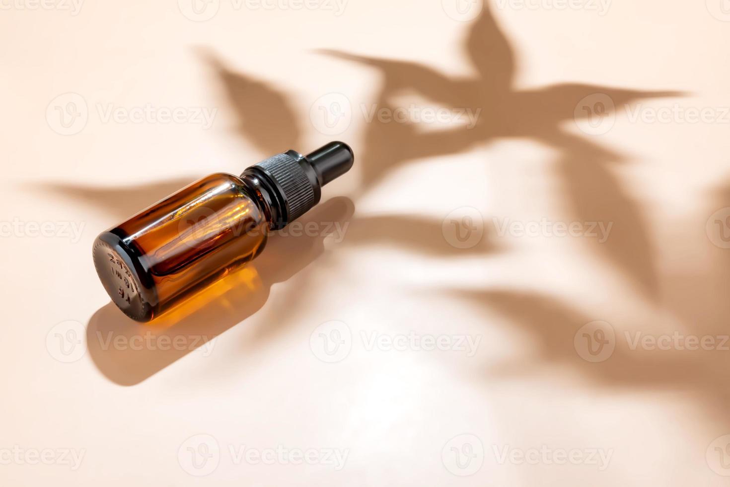 Amber bottle with cannabis oil used for medical purposes on beige background with daylight and the shadow of a hemp leaf. Soothing cbd oil. Alternative Medicine, mockup with copy space photo