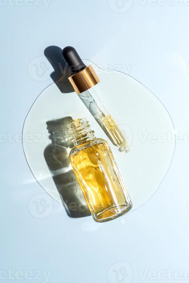 Face beauty oil spilled out of the dropper bottle on blue background. Concept of skin care serum. Unbranded product packaging photo