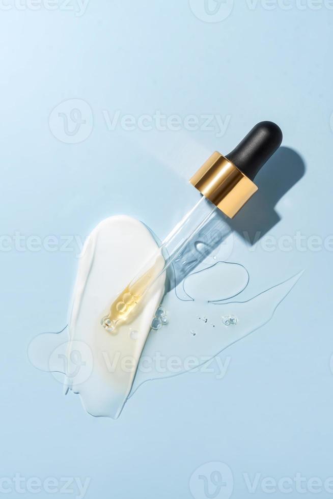 Pipette with fluid retinol acid and cosmetic smear on blue background. Cosmetics and healthcare concept closeup. Dose of serum, retinol with air bubbles. Flat lay. Luxury beauty product presentation photo