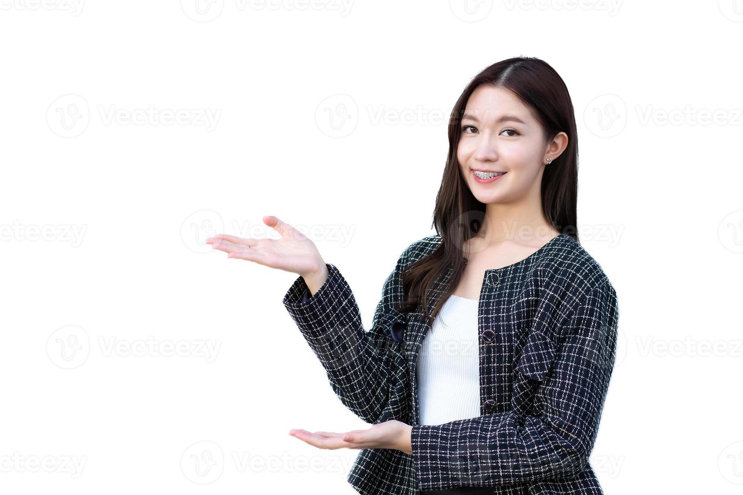 Asian professional working woman who wears black suit with braces on teeth is pointing hand to present something smiling standing confidently isolated on white background. photo