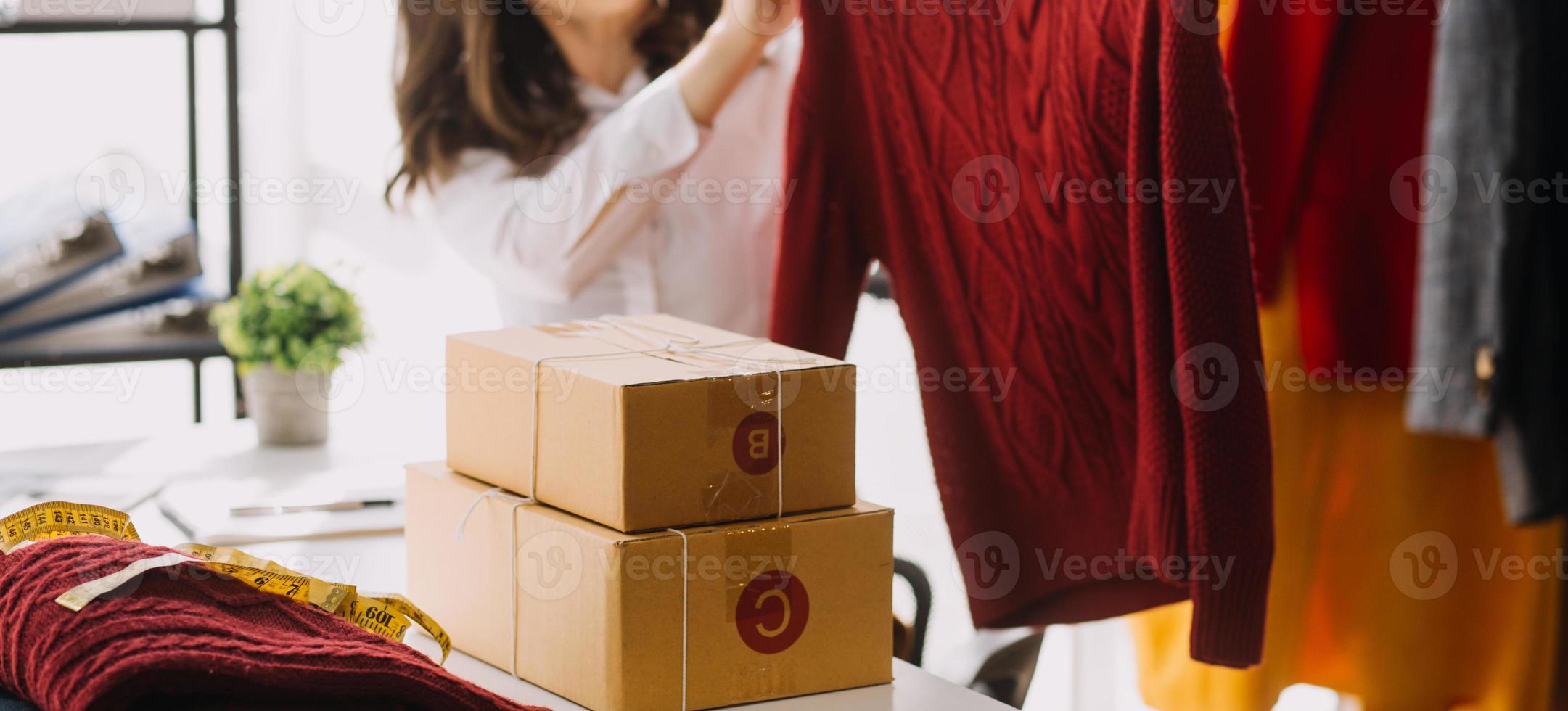 Beautiful lady blogger showing clothes in front of the camera to recording vlog video live streaming at her shop. Online Shopping Cart notion. photo