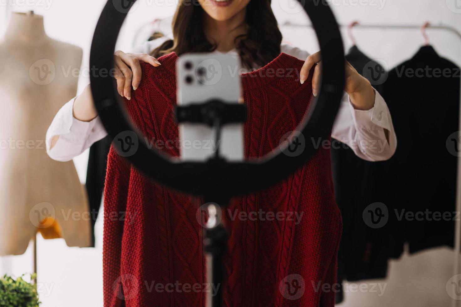 Beautiful lady blogger showing clothes in front of the camera to recording vlog video live streaming at her shop. Online Shopping Cart notion. photo