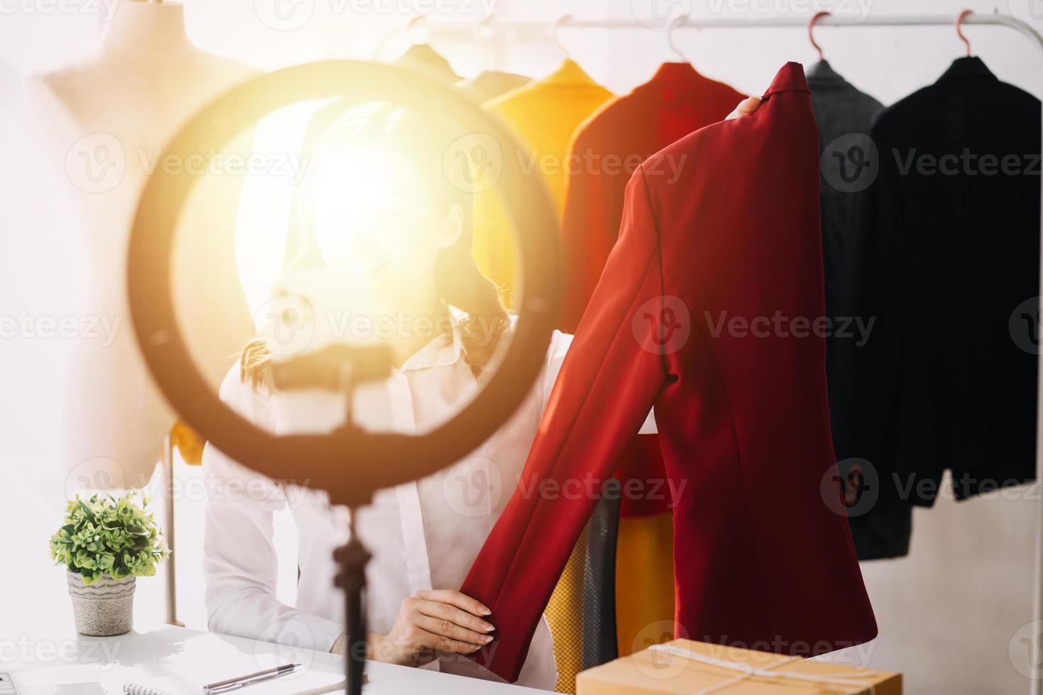 Beautiful lady blogger showing clothes in front of the camera to recording vlog video live streaming at her shop. Online Shopping Cart notion. photo