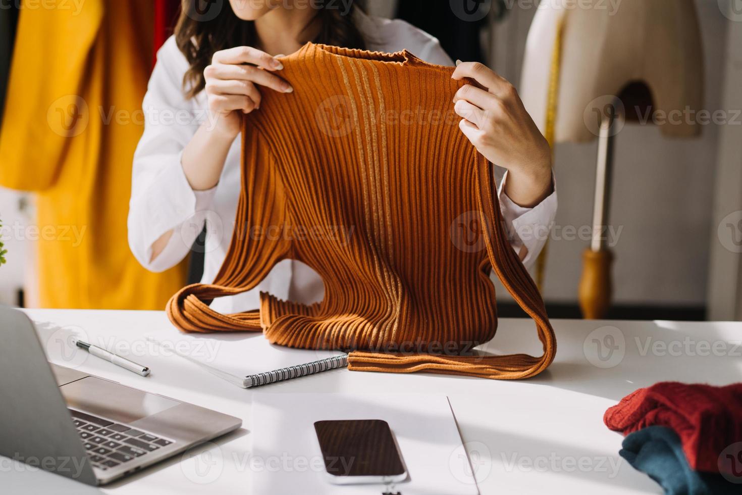 Beautiful lady blogger showing clothes in front of the camera to recording vlog video live streaming at her shop. Online Shopping Cart notion. photo