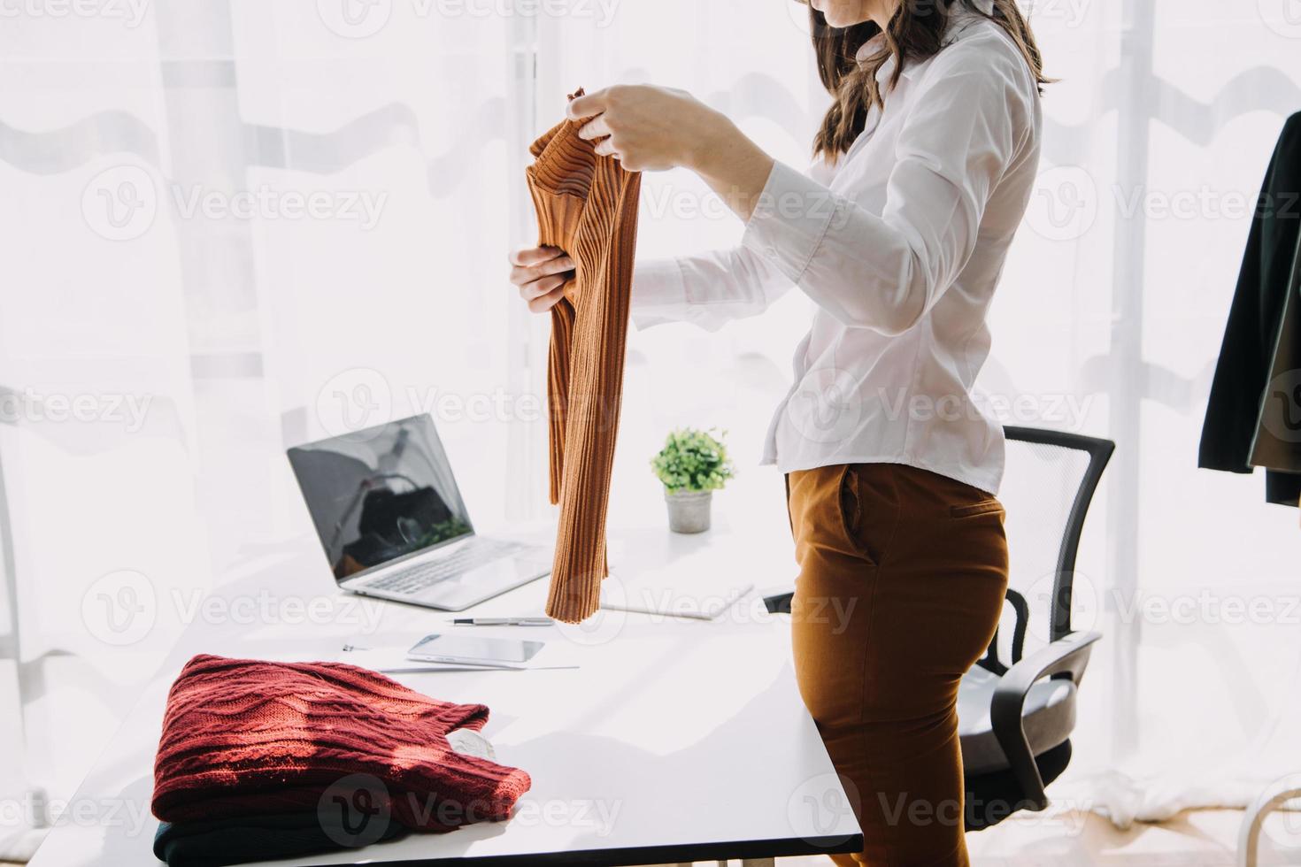 Beautiful lady blogger showing clothes in front of the camera to recording vlog video live streaming at her shop. Online Shopping Cart notion. photo