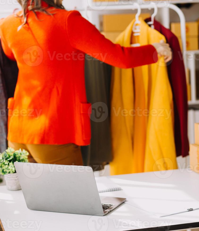 Beautiful lady blogger showing clothes in front of the camera to recording vlog video live streaming at her shop. Online Shopping Cart notion. photo