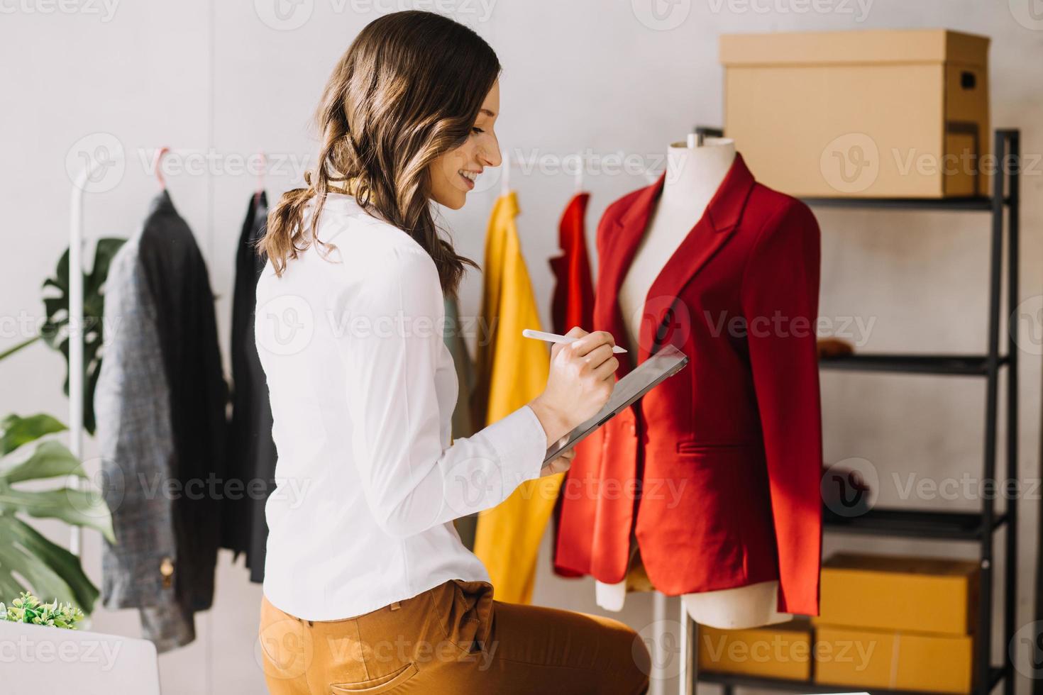 Beautiful lady blogger showing clothes in front of the camera to recording vlog video live streaming at her shop. Online Shopping Cart notion. photo