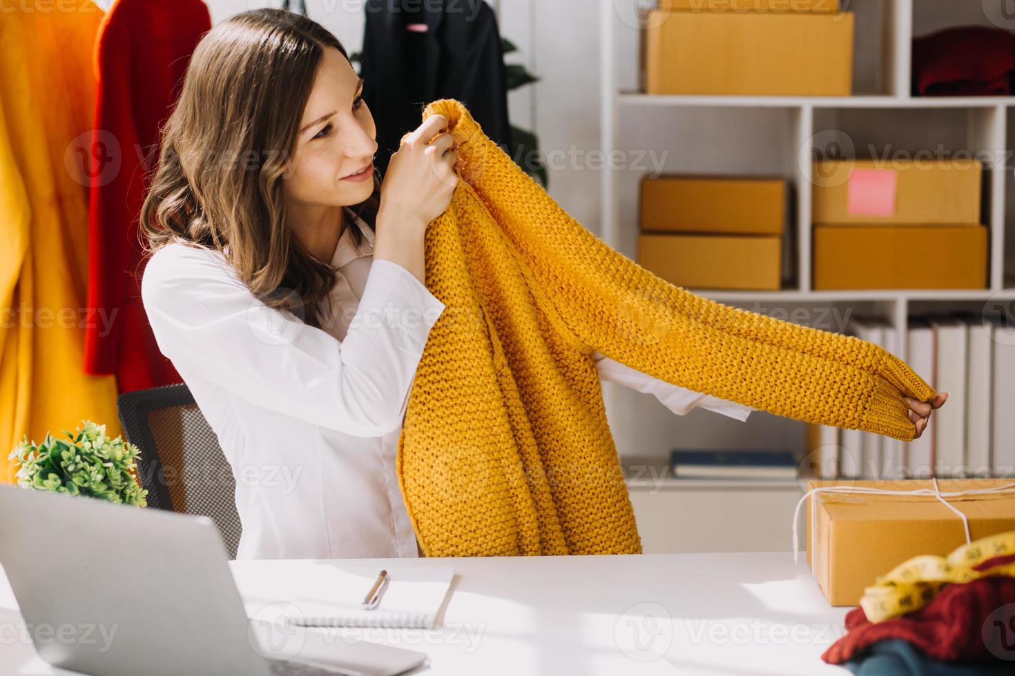 Beautiful lady blogger showing clothes in front of the camera to recording vlog video live streaming at her shop. Online Shopping Cart notion. photo