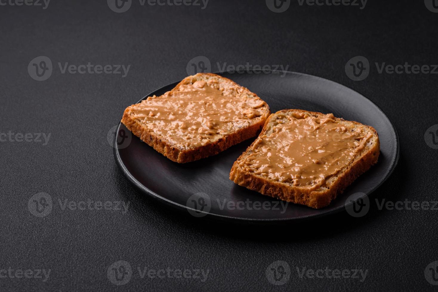 Nutritious sandwich consisting of bread and peanut butter on a black ceramic plate photo