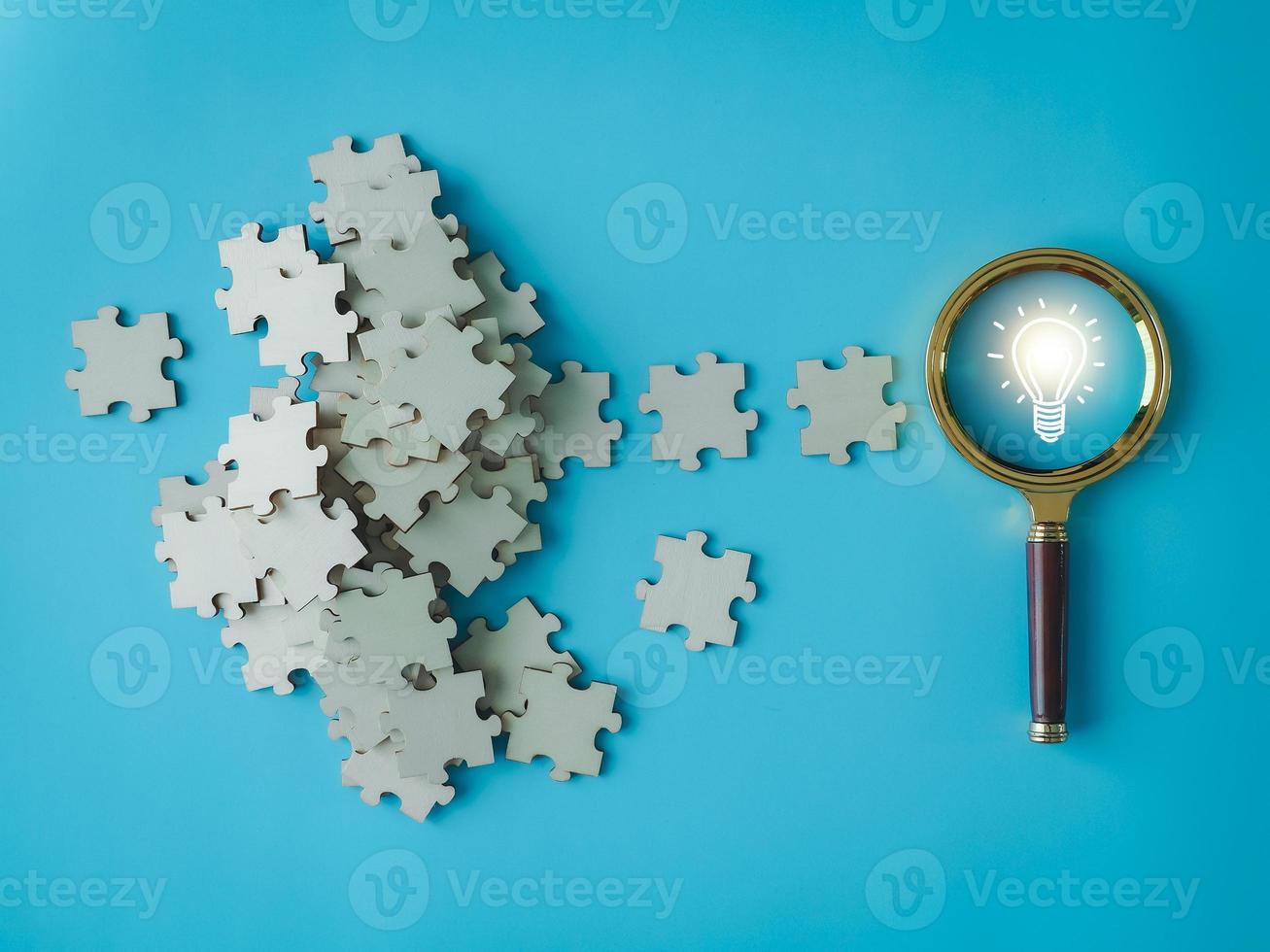 light bulb on a magnifying glass There is a pile of jigsaw puzzles. generating new ideas new business ideas photo
