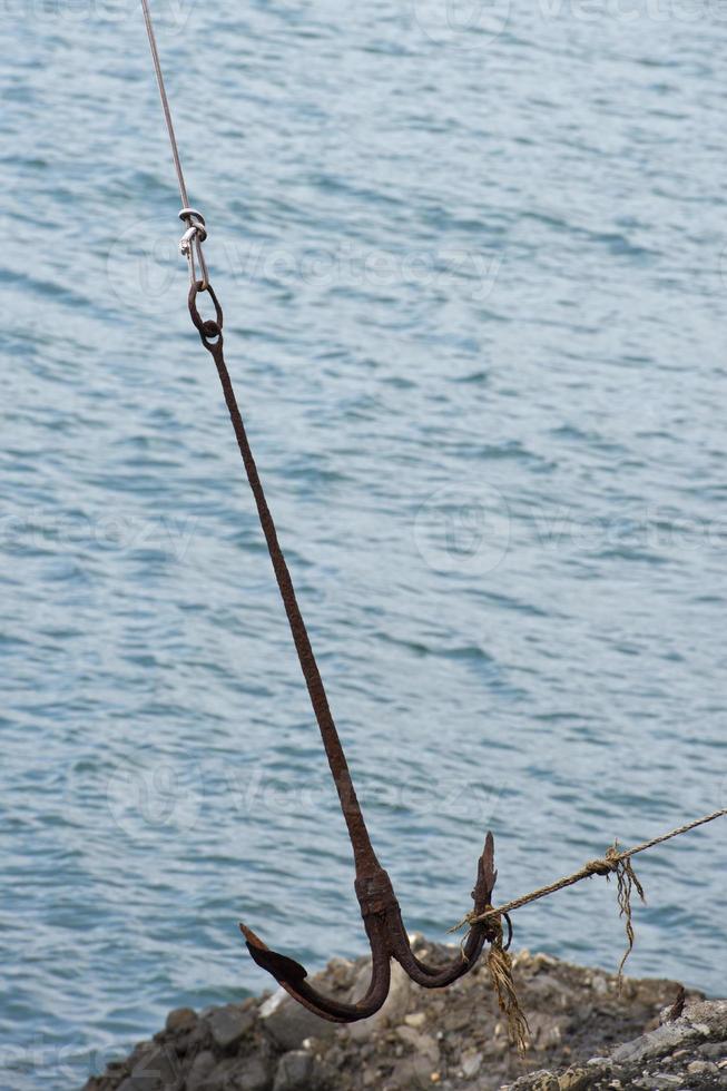 Big Anchor hanging on rocks near the sea photo