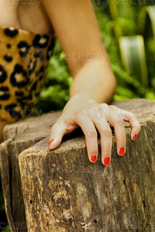 un hembra mujer mano con rojo uñas propensión en madera con verde antecedentes foto
