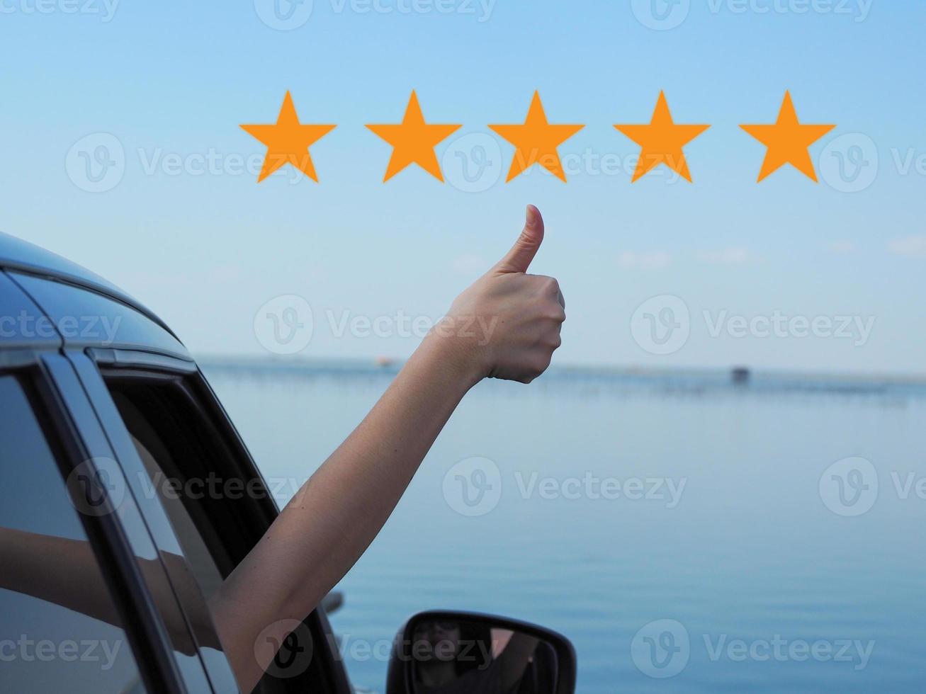 Hand of a girl with thumbs up, with five-star icon, comes out of the car, satisfaction rating. photo