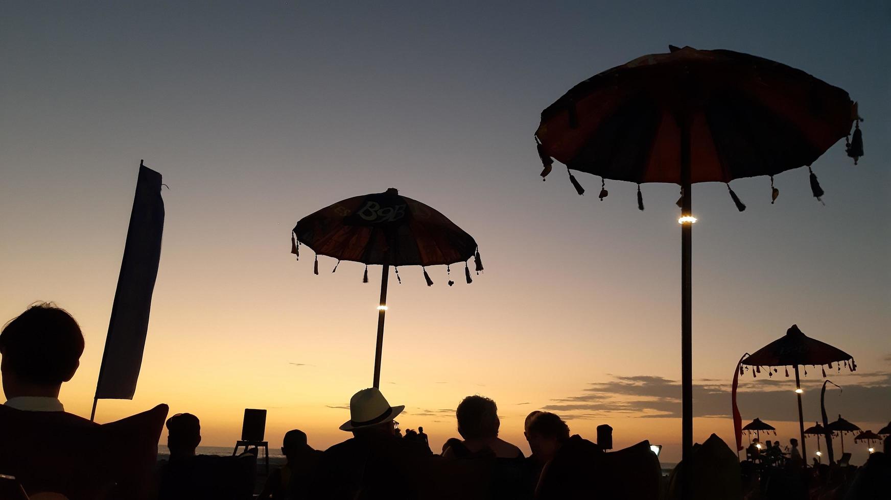 Silhouette People enjoying the sunset view on double six beach in Bali and sitting on sofa cushions and under Balinese umbrellas, November 8, 2019 photo