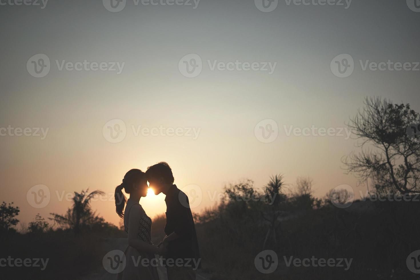 The silhouette couple for prewedding, with a beautiful sunset view and silhouette of hill background with tree and grass photo