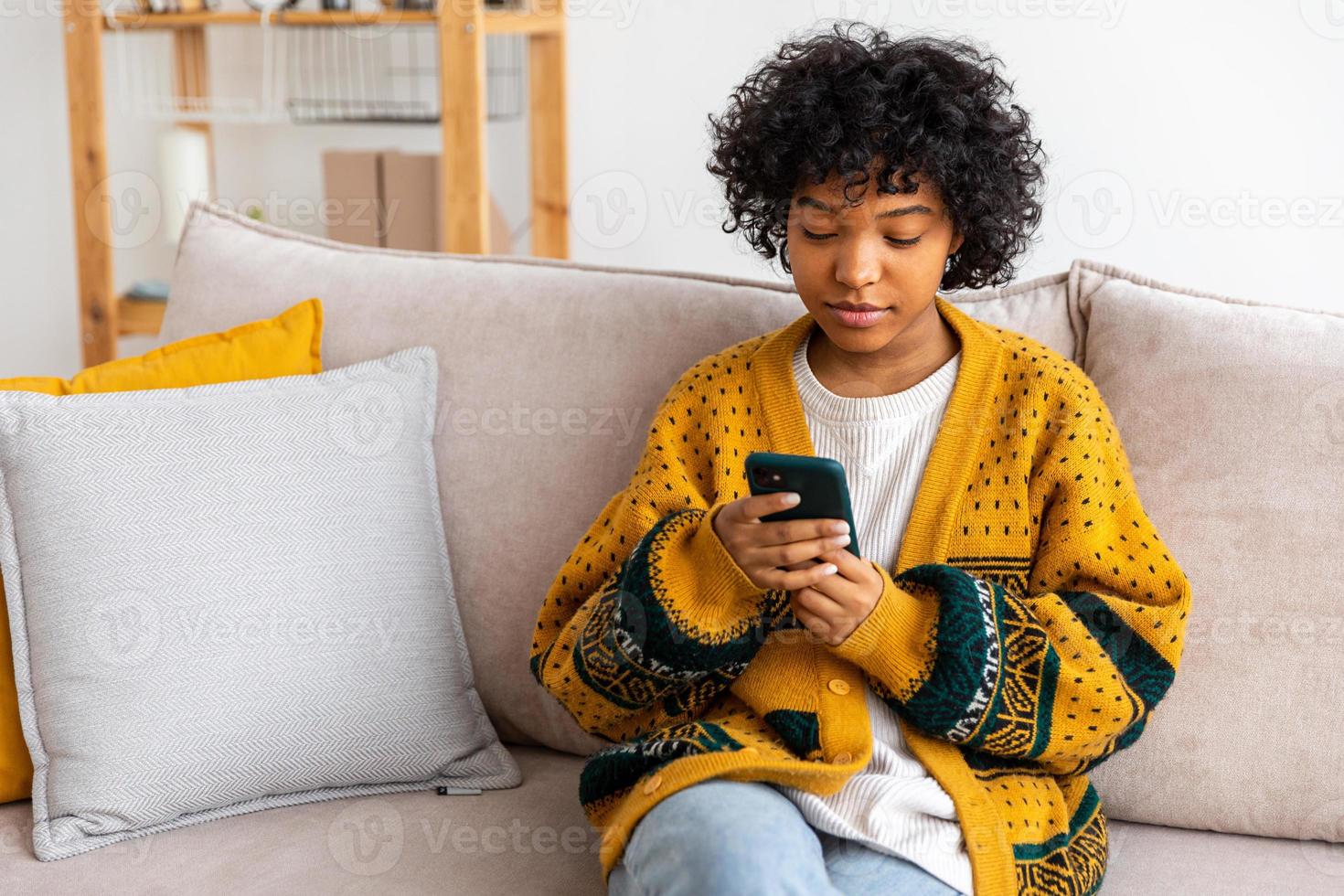 African girl holding smartphone touch screen typing scroll page at home. Woman with cell phone surfing internet using social media apps playing game. Shopping online Internet news cellphone addiction. photo