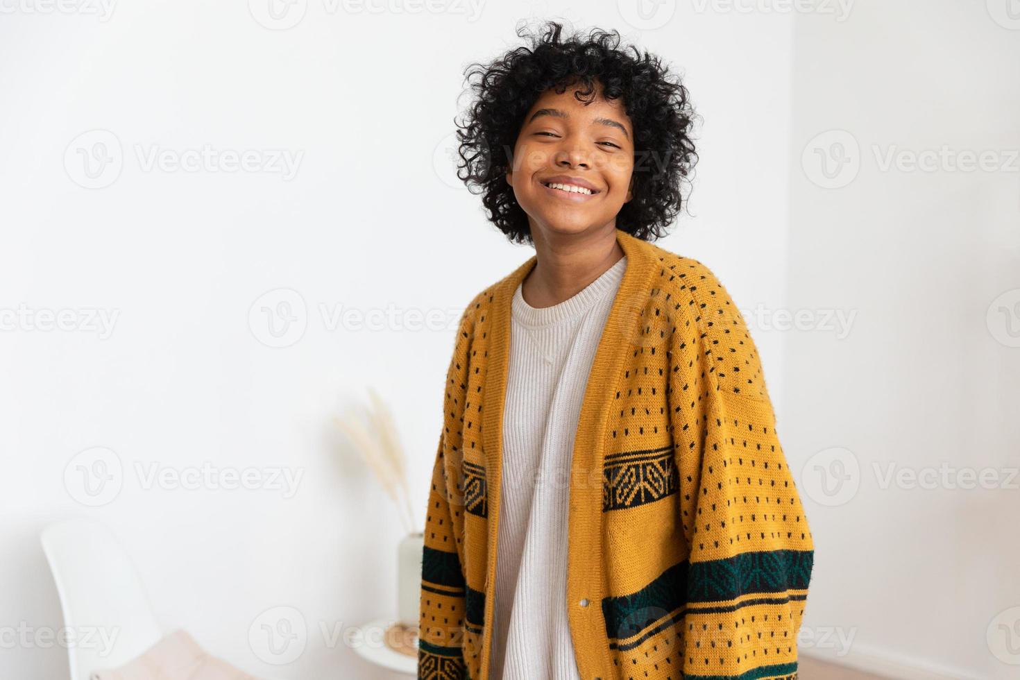 Beautiful african american girl with afro hairstyle smiling at home indoor. Young african woman with curly hair laughing in living room. Freedom happiness carefree happy people concept. photo