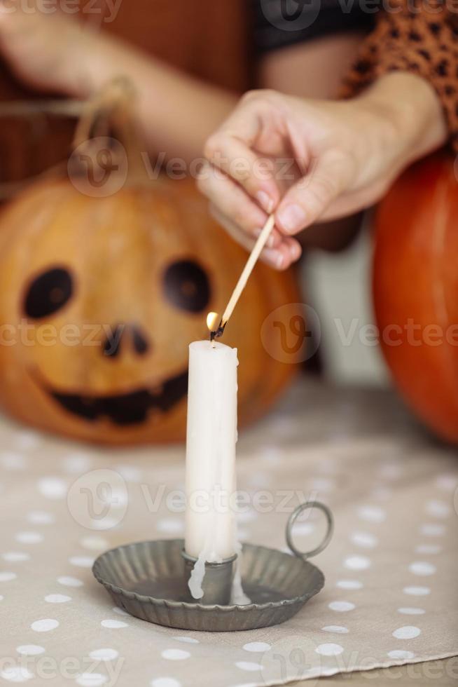 holidays and leisure concept - woman's hand with matches lighting candles at home on halloween. painted pumpkins on a background. horror theme and Hallowe'en. photo