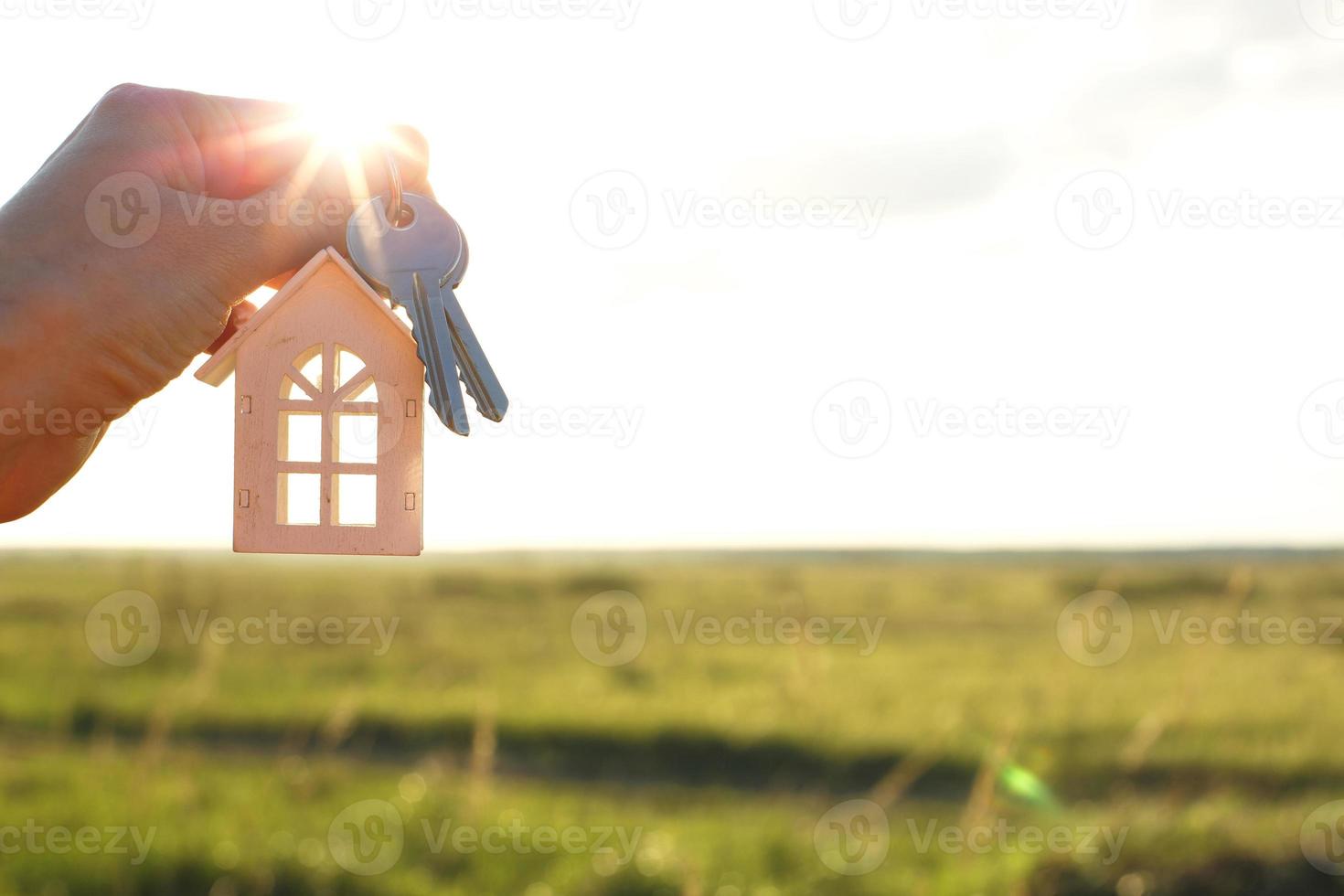 blanco de madera figura de un casa y llaves en mano en contra el antecedentes de el cielo y campo. sueño de tu hogar, edificio un cabaña en el campo, plan y diseño, entrega de el proyecto, foto