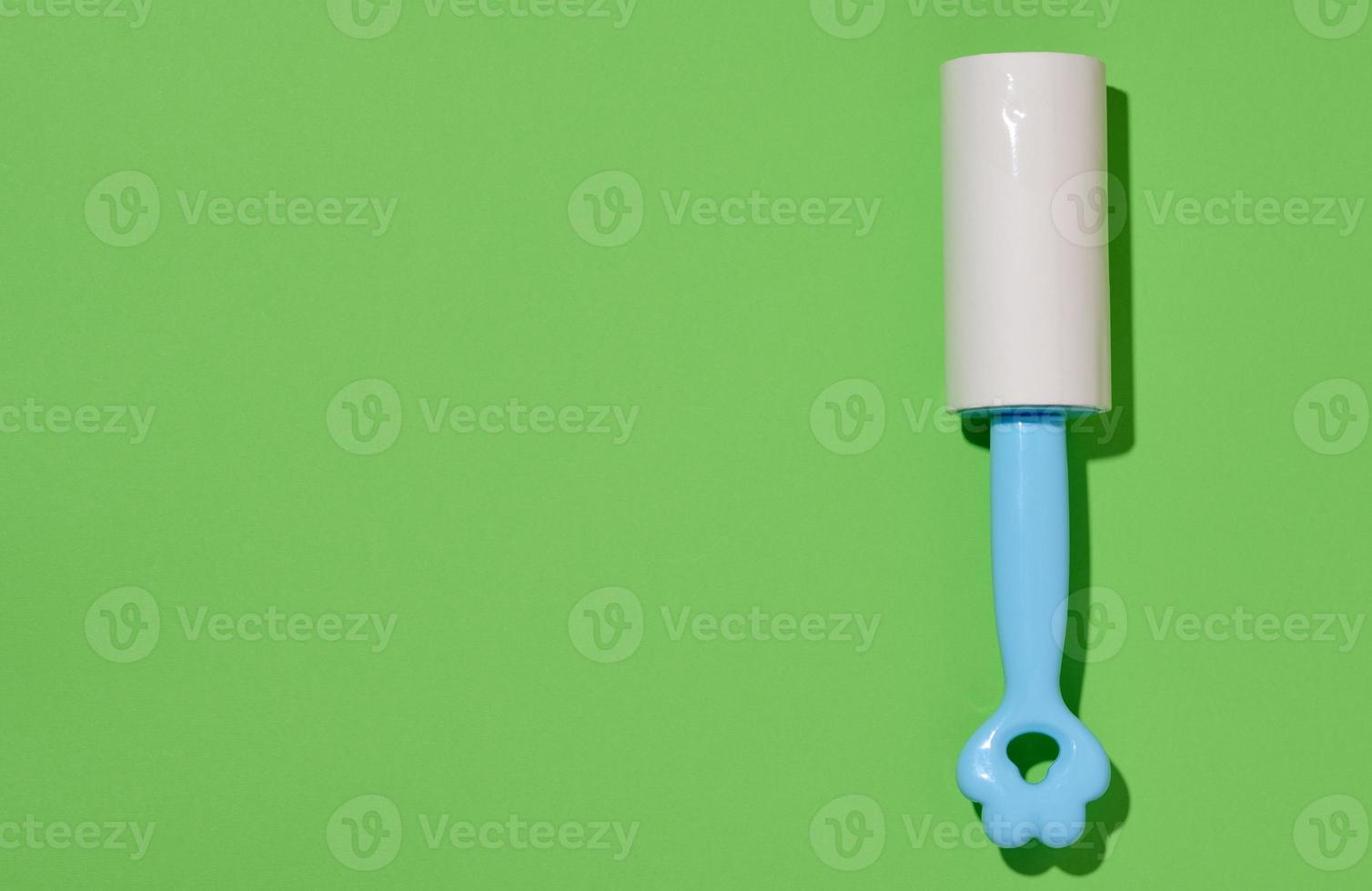 Roller with sticky tape for cleaning clothes on a green background, top view photo