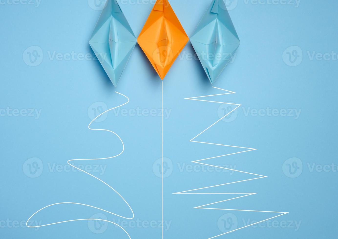 Three paper boats with different trajectories on a blue background, concept of goal achievement differences, effectiveness photo