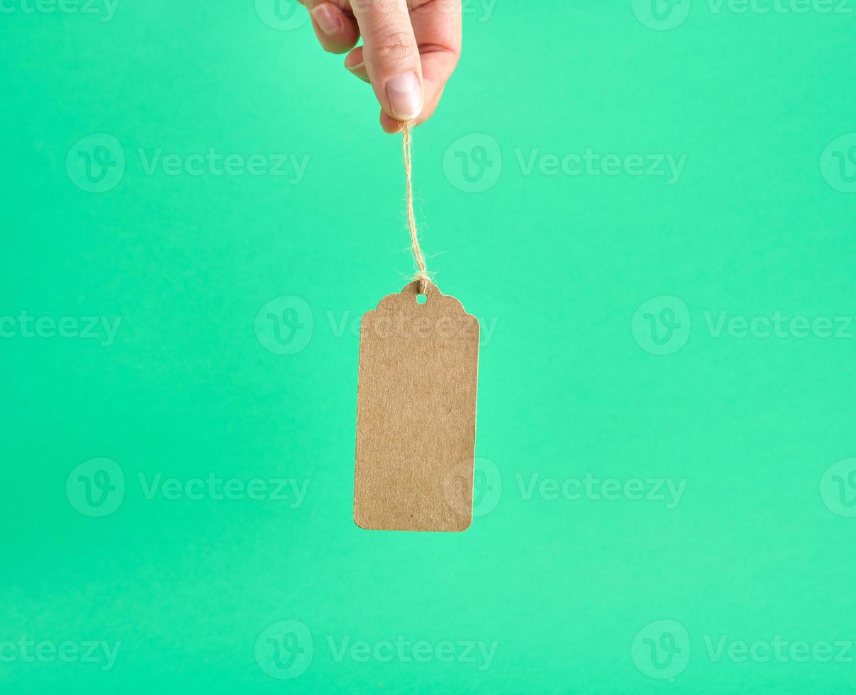 female hand holding a paper brown blank tag on a rope photo