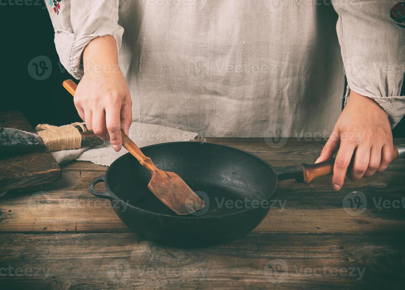 women's hands hold a round black pan and a wooden spatula photo