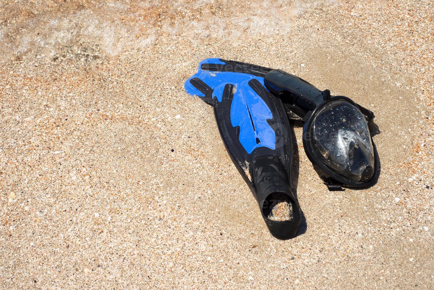 Blue flippers and mask for snorkeling on the sand. Sea wave with bubbles. photo