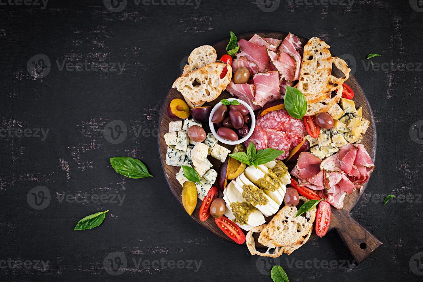 Antipasto platter with ham, prosciutto, salami, blue cheese, mozzarella with pesto and olives on a wooden background. Top view, overhead photo