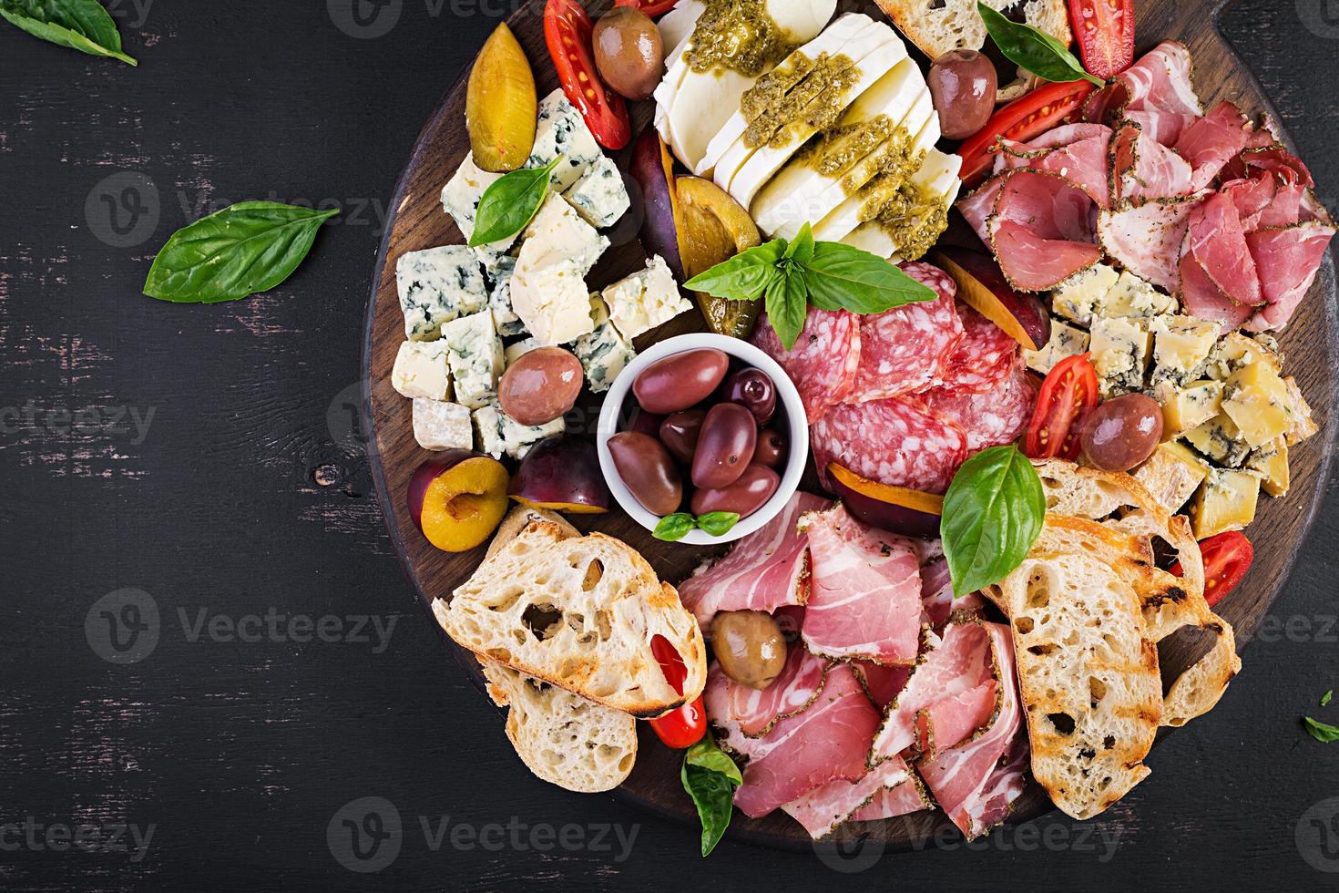Antipasto platter with ham, prosciutto, salami, blue cheese, mozzarella with pesto and olives on a wooden background. Top view, overhead photo