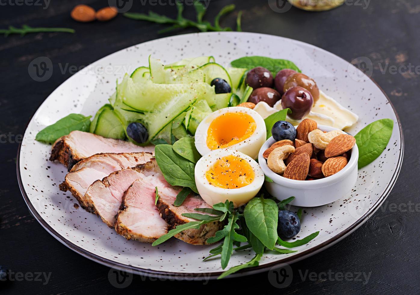 Ketogenic diet. Keto brunch. Boiled egg, pork steak and olives, cucumber, spinach, brie cheese, nuts and blueberry. photo
