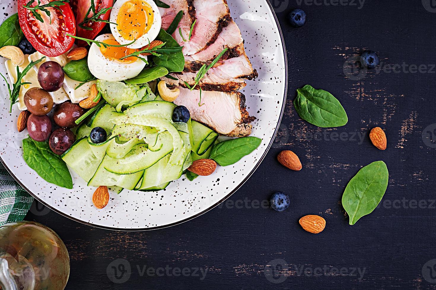 Ketogenic diet. Keto brunch. Boiled egg, pork steak and olives, cucumber, spinach, brie cheese, nuts and tomato. Top view photo
