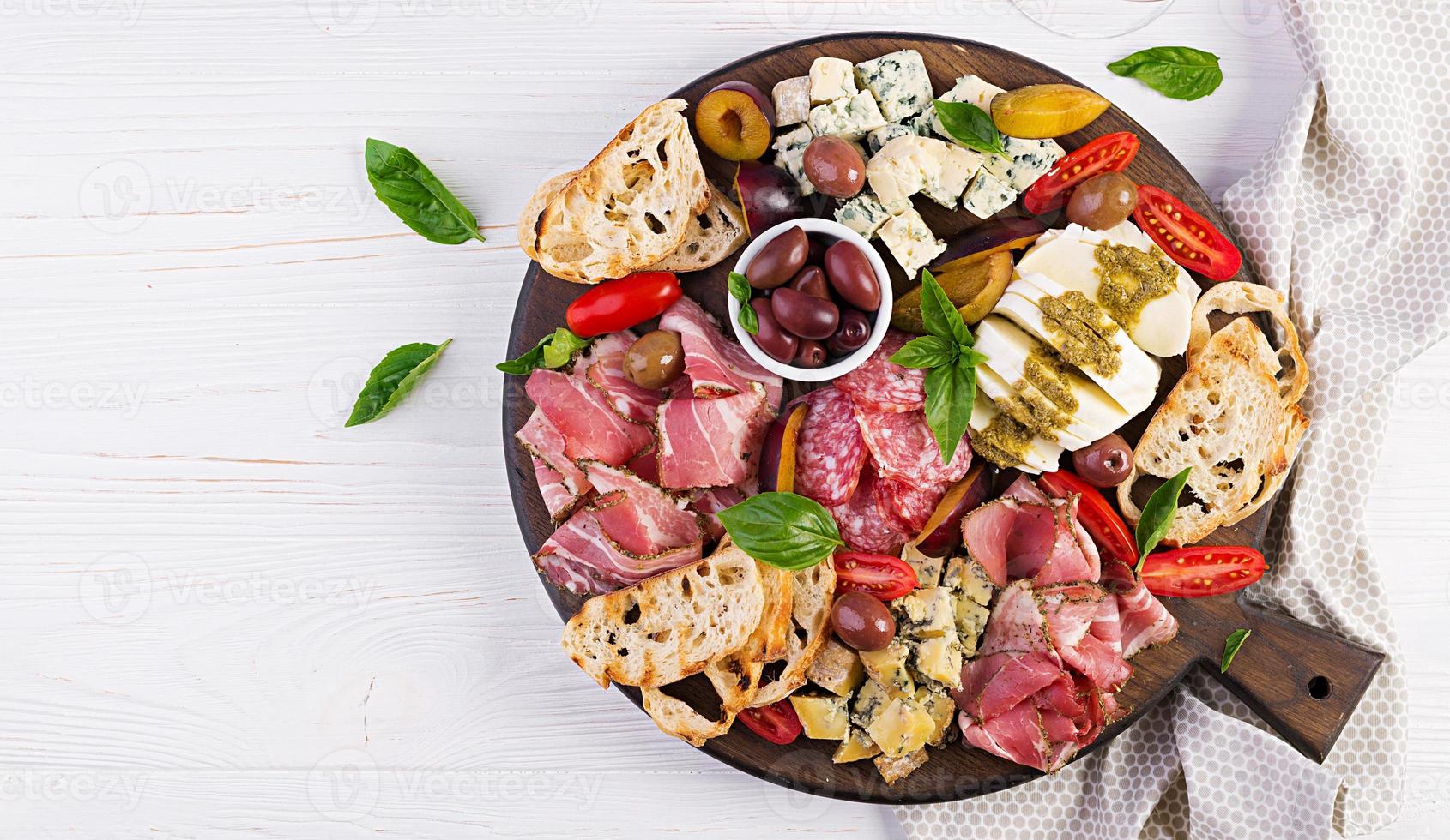 Antipasto platter with ham, prosciutto, salami, blue cheese, mozzarella with pesto and olives on a wooden background. Top view, overhead photo