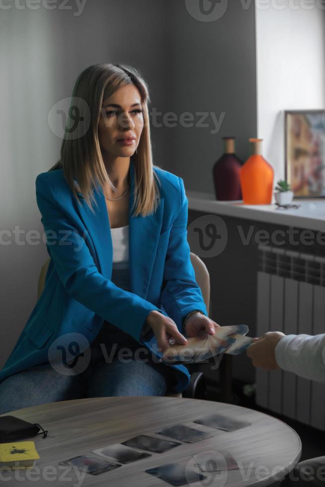 A young beautiful woman psychologist leads a client reception, using metaphorical tarot cards. Universe tips, signs and answers to questions. photo